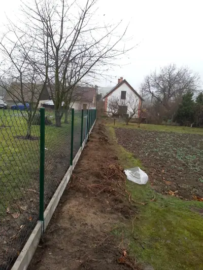 Zelený pletivový plot s podhrabovými deskami podél zahrady