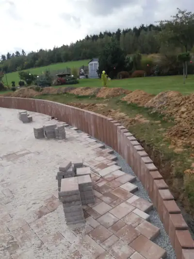 Oblouková plocha z červenohnědé dlažby lemovaná palisádou, při pokládce