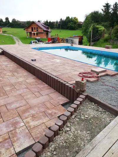 Dlažba kolem bazénu v cihlovém odstínu s obrubou z palisád