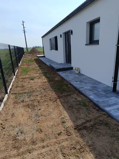 Chodník ze šedé dlažby kolem domu a panelový plot