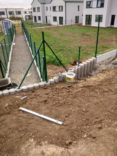 Zelený pletivový plot podél štěrkové cesty a obruba z palisád