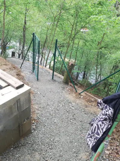Pletivový plot ve svahu u lesa a štěrková cesta