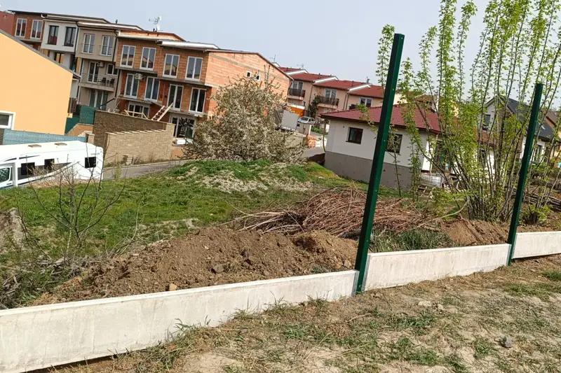 Zelený panelový plot s betonovými podhrabovými deskami u nových domů