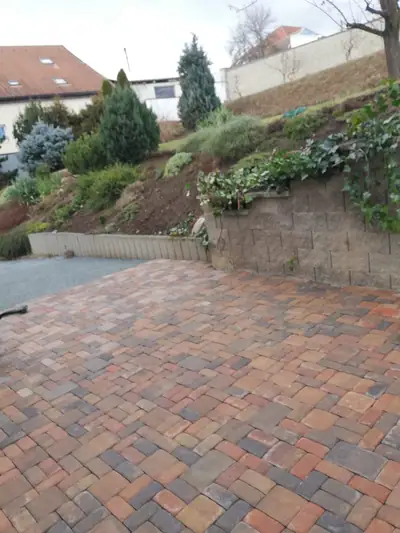 Dvůr z červenohnědé dlažby pod opěrnou zídkou se skalkou