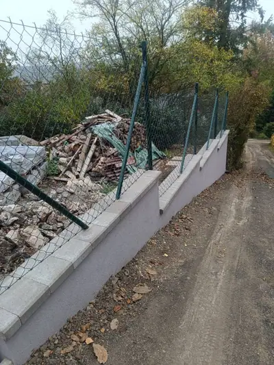 Omítnutá opěrná zídka s krycími deskami a pletivový plot podél štěrkové cesty