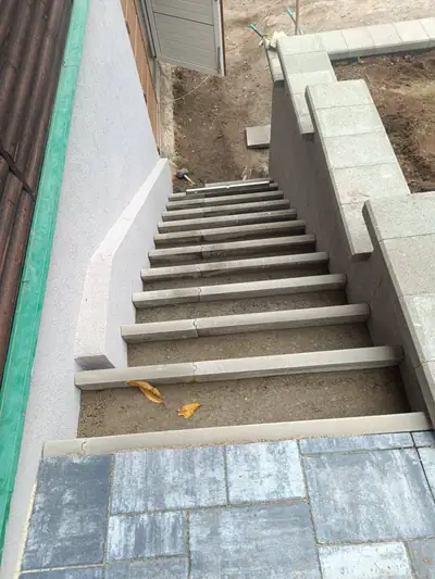 Betonové schody při pokládce mezi omítnutou zdí a zdí z tvárnic, dole dlažba v šedomodrém melíru